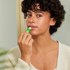 Woman using Weleda Skin Food lip Balm