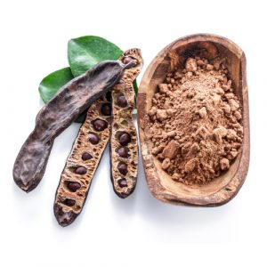 Carob pods and carob powder in the wooden bowl